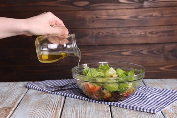 Woman pouring oil onto tasty salad at color wooden table, closeup