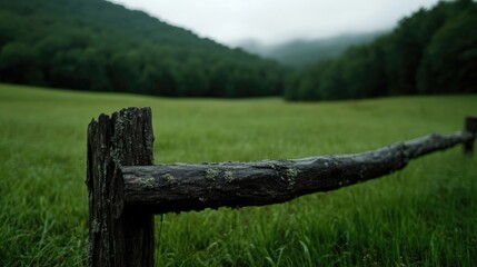 Rustic wooden fence in a lush green meadow, misty mountains in the background