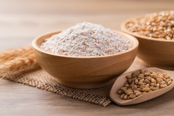 Whole wheat flour with wheat grain in bowl on wooden background