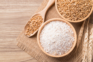 Whole wheat flour with wheat grain in bowl on wooden background, Table top view