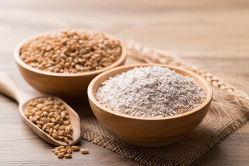Whole wheat flour with wheat grain in bowl on wooden background