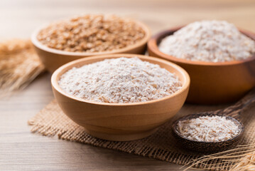 Whole wheat flour with wheat grain in bowl on wooden background