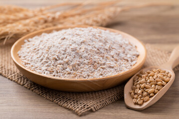 Whole wheat flour with wheat grain on wooden background