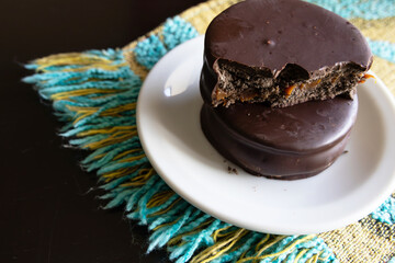 Two dark chocolate alfajores photographed from top to bottom, one is halfway showing the dulce de leche filling and the other is whole
