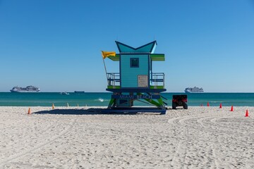 A lifeguard tower stands on Miami Beach, Florida, USA, with a yellow flag indicating caution. The lifeguard uses an ATV to patrol the beach, ensuring swimmer safety.