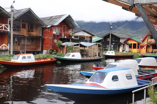 Scenic view of traditional boats moored along the shores of La Cocha Lagoon in Pasto, Colombia, with wooden houses and misty mountains in the background