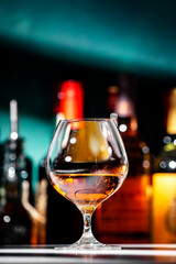 French Armagnac cognac in snifter glass and bottles of strong drinks on dark green background, hard light