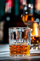 American bourbon whiskey in glass with bottles of strong drinks on dark green background
