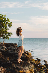 Young woman in blue jeans short at the beach. Beautiful colorful sunset at the beach. Summer vacation in Florida. Key West, Florida, US. Young lady is posing at the ocean on sunrise