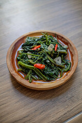 Cah kangkung or tumis kangkung or Vegetable kale, food from Indonesia, on a wood plate