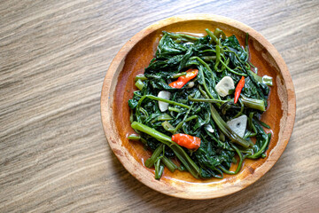 Cah kangkung or tumis kangkung or Vegetable kale, food from Indonesia, on a wood plate
