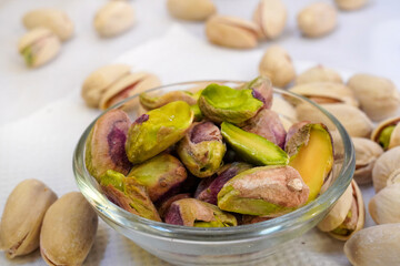 Salted pistachios in a glass bowl and scattered around on a white background, isolated, side view, crunchy roasted nuts,tasty,nutritious snack, healthy organic food, high-protein.