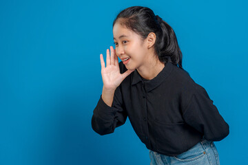 Young Asian woman smiling while cupping hand beside mouth, expressing joy and communication....