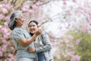 Fototapeta premium A joyful moment between an elderly woman and a young woman as they laugh together beneath blooming pink trees. Their warm embrace and shared laughter reflect the deep love of family and nature.