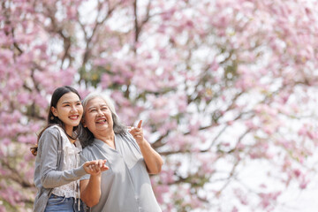 Fototapeta premium A young woman and an elderly woman share a heartfelt moment beneath blooming pink trees. Surrounded by spring’s beauty, their warm expressions reflect love, connection, and peaceful togetherness.
