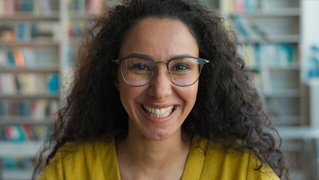 Happy Latino Arabian Hispanic woman girl student teenager looking at camera smile adjust hair library high school academy smart university teacher educational books confident female reader intelligent