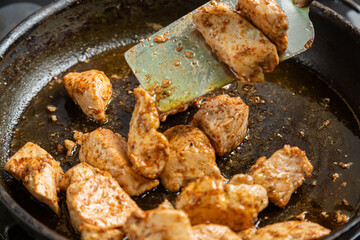 Chicken fillet pieces are fried in a frying pan in spices and turned over