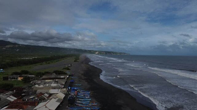 Scenic coastal landscape with waves gently rolling to the black sandy beach under dramatic sky on Depok Beach Yogyakarta