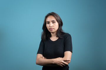 A thoughtful Indonesian woman in a black shirt stands with arms crossed, looking serious and...