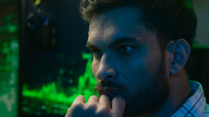 Concentrated focused Arabian Indian man analysing chart crypto currency businessman business programmer IT specialist coder trader male ethnic guy wearing glasses eyeglasses in night office working