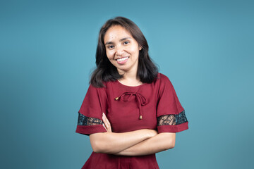 Young Indonesian woman in a red dress smiles brightly at the camera with arms crossed. Perfect for...