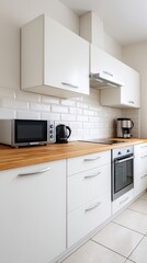 A modern kitchen featuring white cabinets, a wooden countertop, and appliances like a microwave, kettle, and coffee maker.