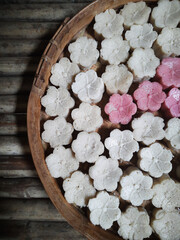 Colorful flower-shaped apem cakes beautifully arranged on a woven bamboo tray, traditionally prepared in rural villages as a beloved Eid al-Fitr treat.