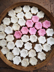Colorful flower-shaped apem cakes beautifully arranged on a woven bamboo tray, traditionally prepared in rural villages as a beloved Eid al-Fitr treat.