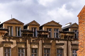 An old tenement house with visible signs of the passage of time. Falling plaster, damaged cornices and neglected windows. The building is in a classic style with triangular pediments above the attic w