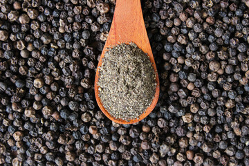 Black pepper powder on wooden spoon with black peppercorns seeds background. Food ingredients. Aromatic spice. Top view