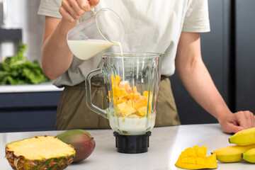Fresh tropical smoothie preparation with mango, pineapple and milk in a modern kitchen