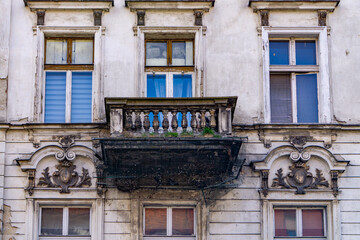 A ruined balcony of an old tenement house with a balustrade on which wild vegetation grows. Falling plaster, bricks and dirt. On the right side there is an old ball of light on a metal pole