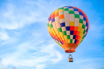 Naklejka premium A colorful hot air balloon soars gracefully through the sky against a backdrop of soft, wispy clouds.