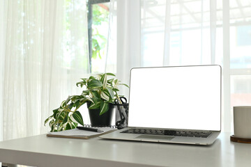 Fototapeta premium A laptop sits on a desk with a plant and a cup. The laptop is open and the screen is blank.