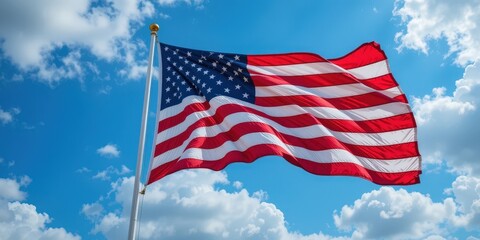 Obraz premium A large American flag, vibrant and billowing, waves majestically against a clear blue sky, its red and white stripes and bright stars symbolizing freedom and patriotism.