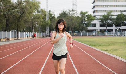 Fototapeta premium focused southeast Asian woman runner is jogging on track in outdoor stadium, embracing healthy lifestyle with determination and motivation, symbolizing wellness and challenge