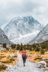 Fototapeta premium A solitary hiker with a backpack navigates a winding trail through a rugged snow blanketed mountain landscape on a cold overcast day