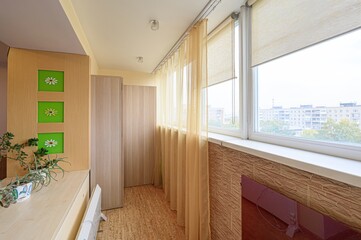 Bright, airy balcony with plants.  Light wood, green accents, and sunny windows create a cheerful, cozy space.
