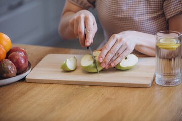 A beautiful brunette woman in the kitchen cuts a green apple in close-up
