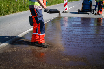 Close-up of construction worker spreading gravel over liquid bitumen on a newly renovated road