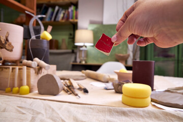 Close-up of a ceramic tile sample in hand against the background of a pottery workshop