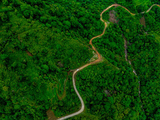 Aerial view of a muddy mountain road cutting through lush green hills during the monsoon season — showcasing the natural beauty of the rainy season in the mountains