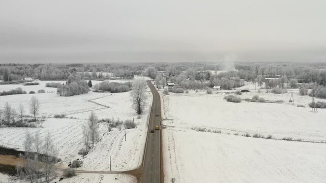 Aerial drone view of a straight countryside road with one car overtaking another one. Frozen winter weather with lots of snow.