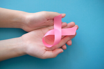 Pink ribbon on a woman's handon and blue background. Breast cancer concept symbolic tape