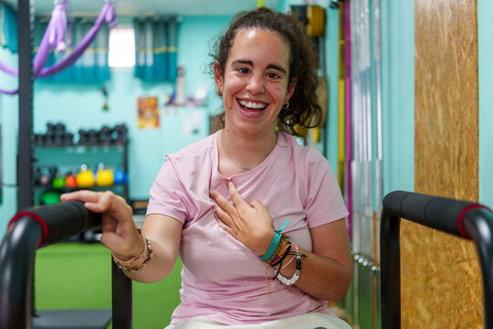 Happy woman with cerebral palsy smiling and training in a gym, holding on to the handles of a fitness equipment