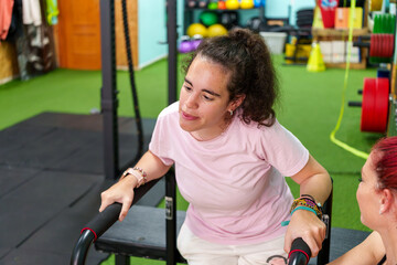 Young woman with cerebral palsy exercising with parallel bars and assisted by her personal trainer...