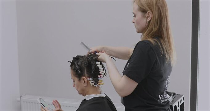 Professional hairdresser working with client, closeup. Hairdresser winding perm rods. Hair curlers.
