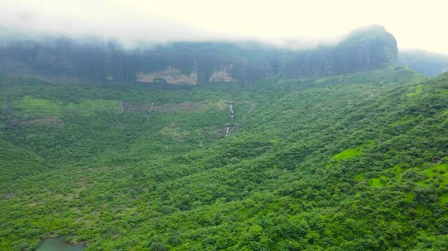 Vibrant green valley with cascading waterfalls amidst mist-shrouded rocky cliffs, epitomizing untouched natural beauty and serenity in wilderness. nature travel. Paine, Nashik, Maharashtra, India