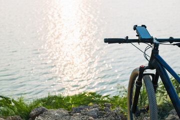 Smartphone and holder attached to the handlebar of a bicycle while parking at the bank of the lake, with sunlight reflects on the surface of the water
