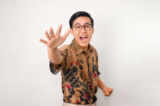 Asian man wearing batik and glasses, shouting and hands making gestures of wanting to reach for something